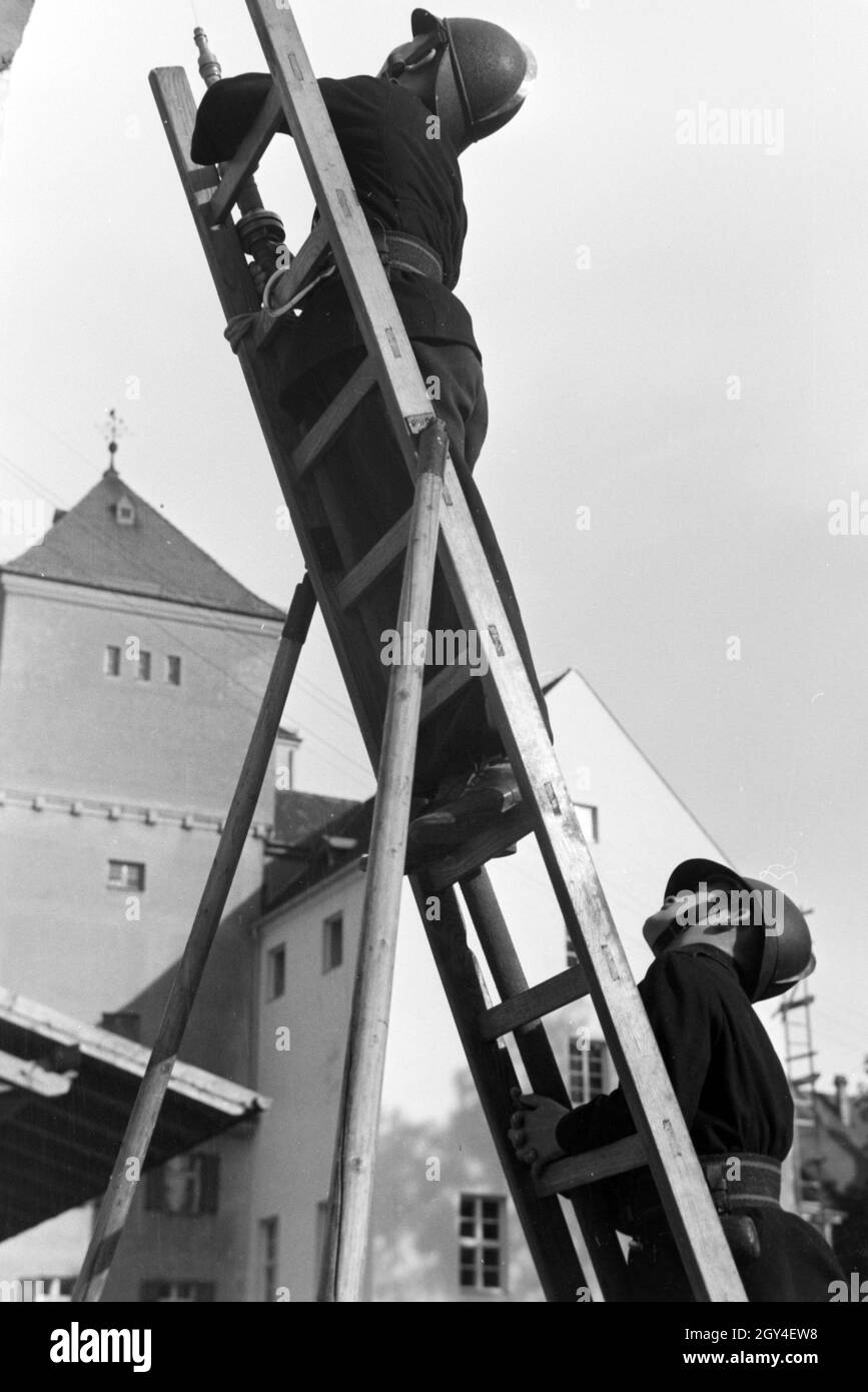 Zwei Jungen von der Kinderfeuerwehr bei einer Feuerwehrübung mit dem  Löschschlauch auf einer Leiter, Deutschland 1930er Jahre. Two boys of the  junior firefighters standing on a ladder with the water hose during