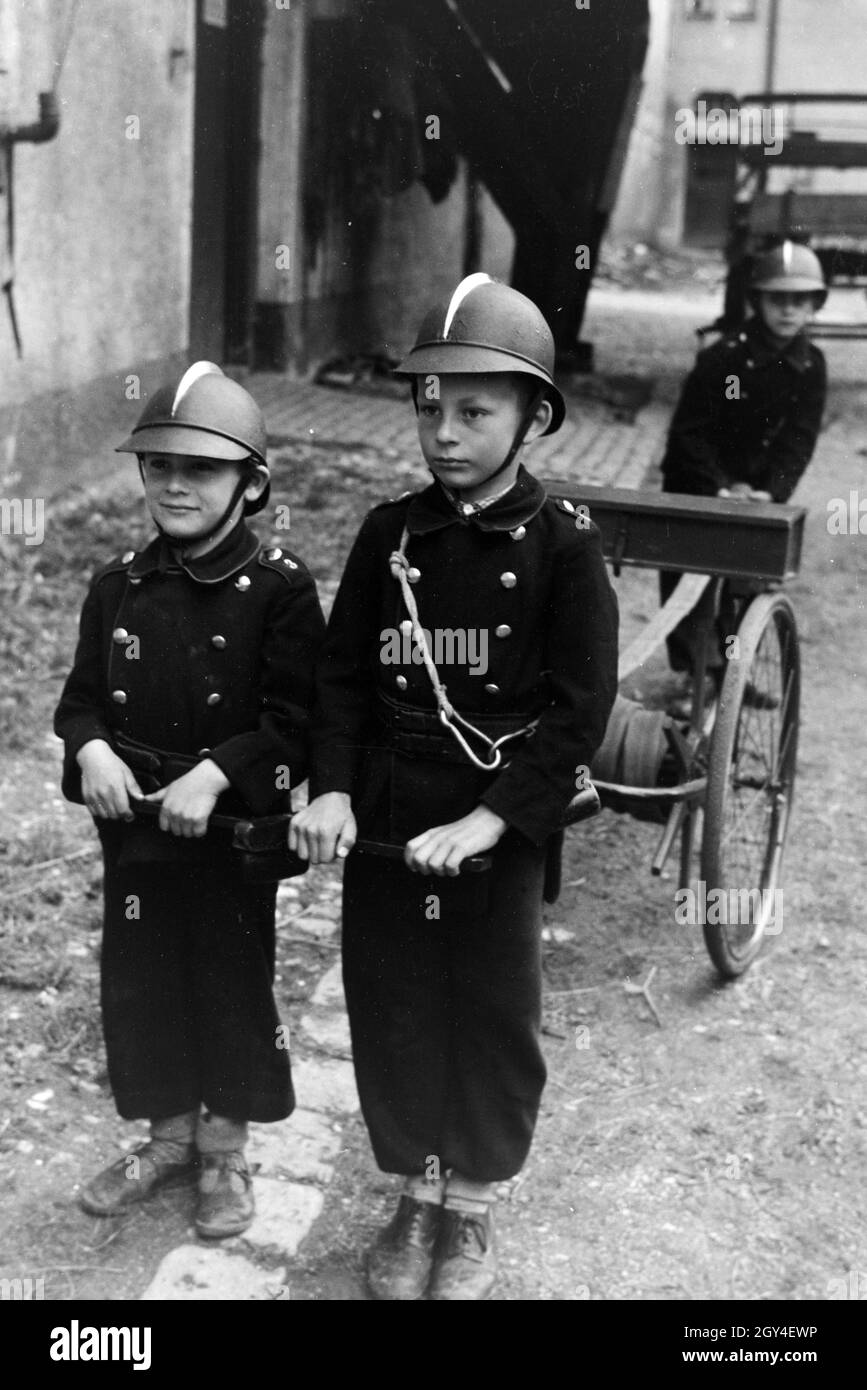 Jungen von der Kinderfeuerwehr bei einem Übungseinsatz mit dem Löschwagen, Deutschland 1930er Jahre. Boys of the junior firefighters during a training holding a hand pump, Germany 1930s. Stock Photo