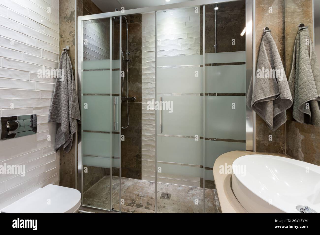 Bathroom in modern style with textured tiles on the floor and walls. Two  showers with glass door, white toilet and towels Stock Photo - Alamy, image size:1300x956