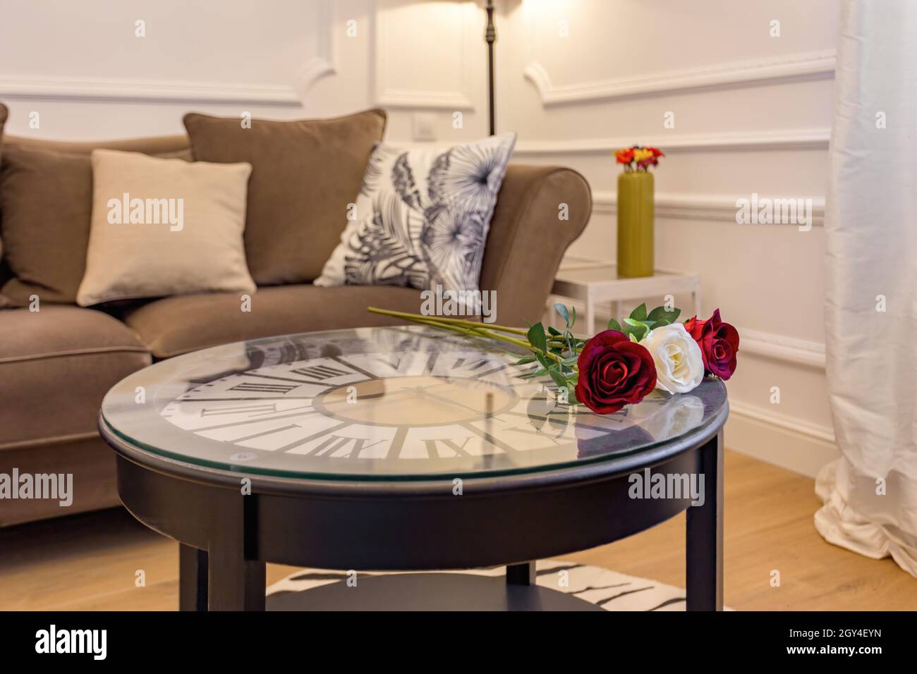 Fresh roses on coffee table with clock inside. Interior of living room with cosy sofa. Stock Photo