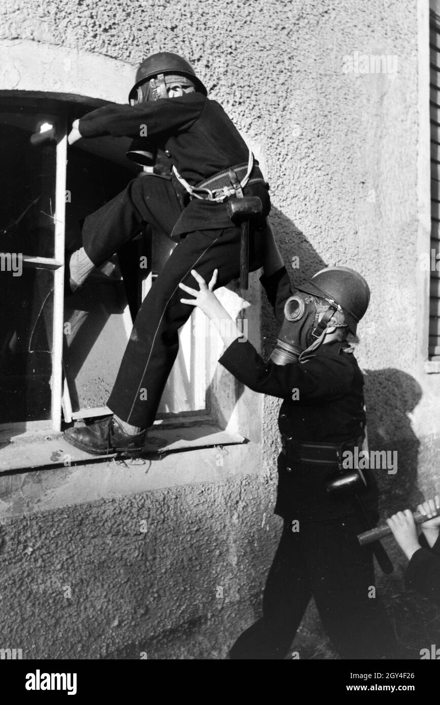 Jungen mit Rauchmasken klettern bei einem Übungseinsatz der Kinderfeuerwehr durch ein fenster, Deutschland 1930er Jahre. Boys with smoke helmets climbing through a window during a training of the junior firefighters, Germany 1930s. Stock Photo