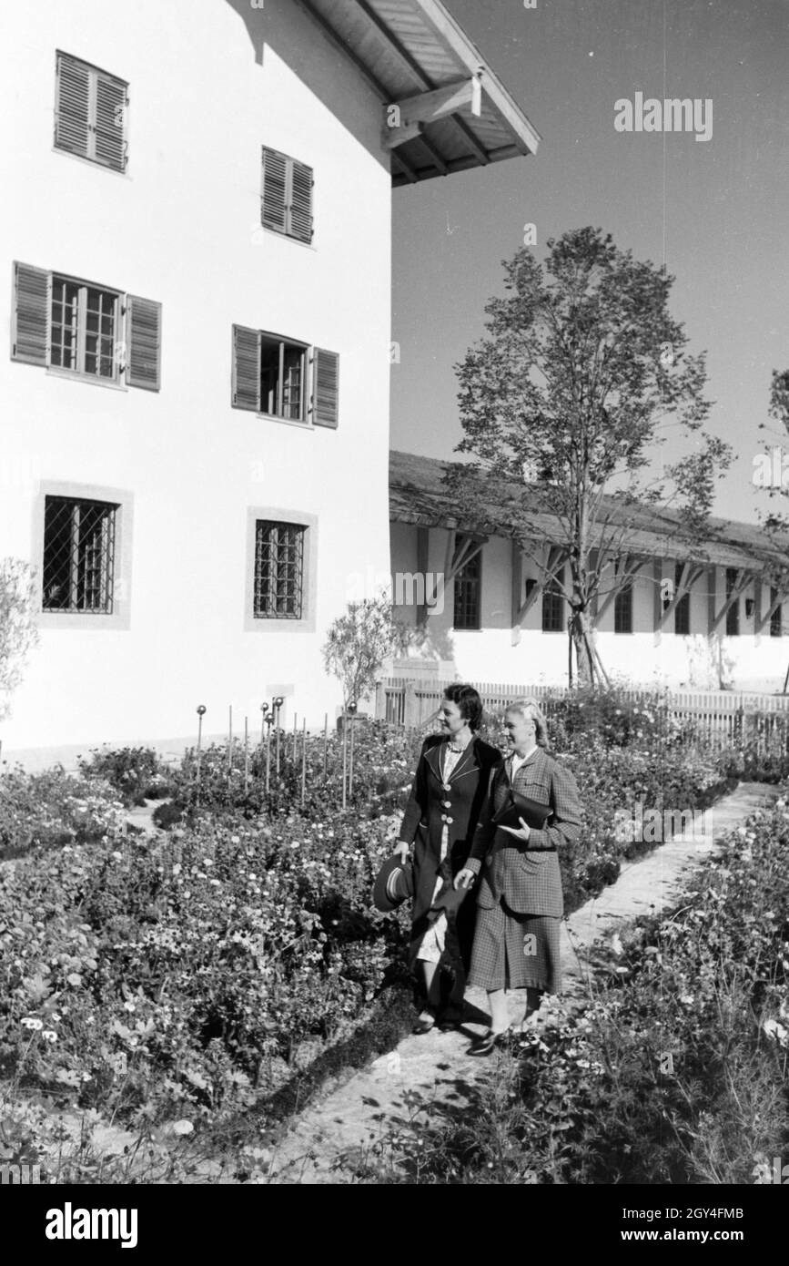 Zwei junge Frauen gehen im Garten des Rathauses am Chiemsee spazieren, Deutschland 1930er Jahre. Two young women are strolling through the city hall garden at the Chiemsee, Germany 1930s. Stock Photo
