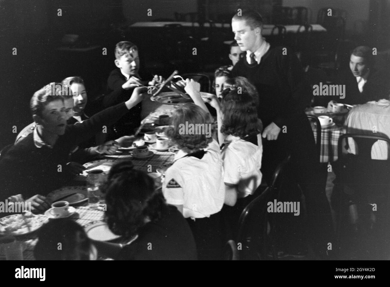 Eine Eiskunstlauf Gruppe der Hitlerjugend in den Uniformen der HJ und des BDM während des Essen nach dem Trainings, Deutschland 1930er Jahre. A figureskating group of the Hitler Youth wearing uniforms of the HJ and BDM during dinner after a training, Germany 1930s. Stock Photo