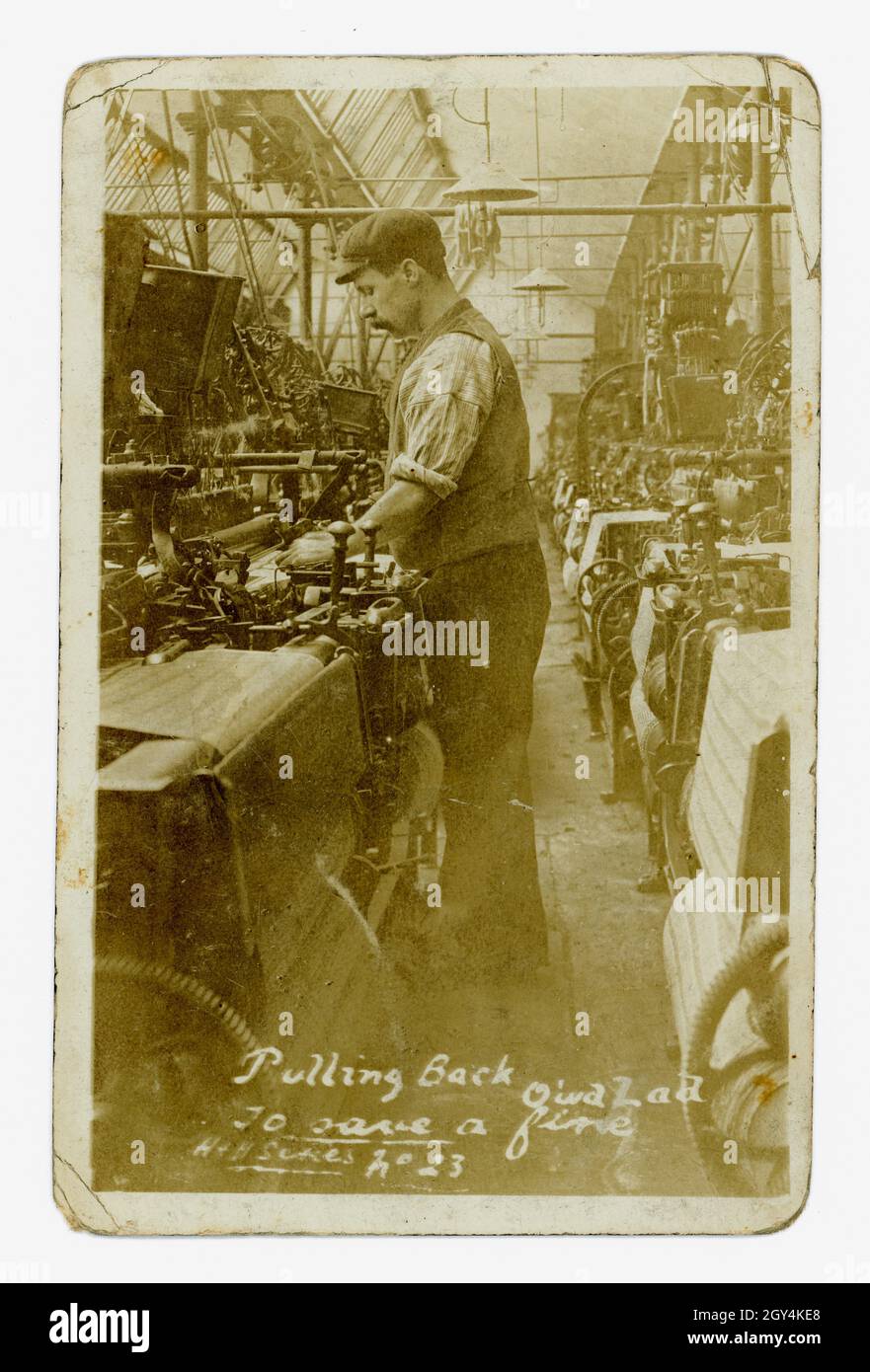 Original Edwardian era postcard entitled 'Pulling Back Quick Lad to Save a Fine' indicative of the poor working conditions of this time  - low wages, unhealthy damp and dusty workplaces, punishments and fines - . Photograph of a young man operating a weaving machine at a cotton mill, Nelson, Pendle, Lancashire, U.K. circa 1905. Stock Photo