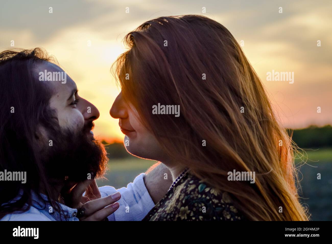 Backlight portrait of a young couple standing to kiss with sunset, he has a  beard and long hair, her long red hair Stock Photo - Alamy