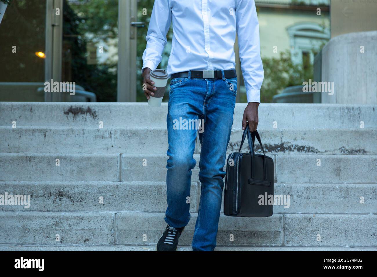 young black business man with no face walking down stairs with glass of coffee leaving work Stock Photo
