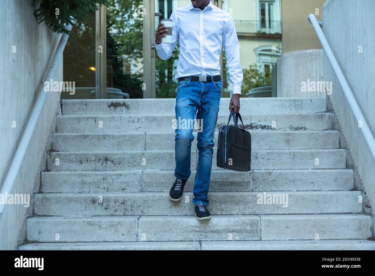 young black man anonymous office worker walking down stairs with satisfaction looking at glass of coffee leaving work Stock Photo
