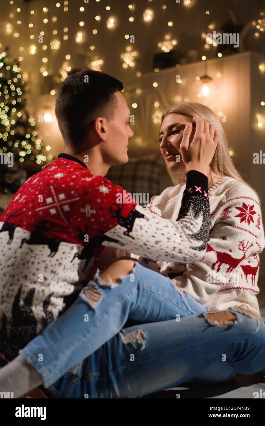 Hugging Sweater Lovely couple sitting on carpet wearing christmas sweater and hugging ...