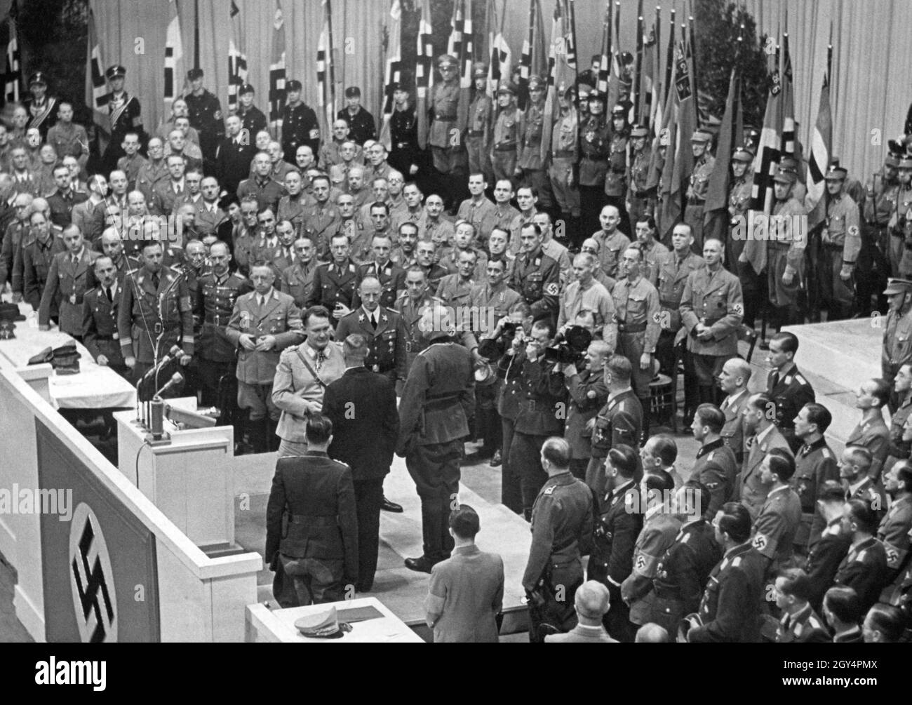 'On October 4, 1942, Thanksgiving Day, Reichsmarschall Hermann Göring (center, at the lectern) gave a ''Thanksgiving Speech'' at the Sportpalast in Berlin-Schöneberg. In the speech he assured to secure food for the ''German people'' in the approaching winter. Behind Göring on the right is Agriculture Minister Herbert Backe, and probably Joseph Goebbels in the center at the bottom of the picture. In the picture, Göring awards the Knight's Cross of the Order of Merit of the War to the farmer leader Ernst Ritter (black suit) and the farmer leader Fritz Leffler (next to him on the right). Stock Photo