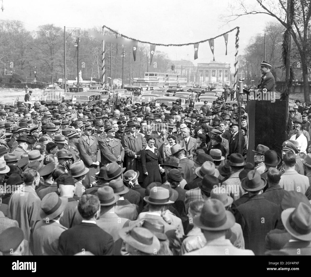 An SA group leader speaks to a large crowd on the East-West axis (today: Straße des 17. Juni) in Berlin-Mitte in 1939. In the audience are members of NSDAP organizations such as the SA or SS. In the background you can see the Brandenburg Gate hung with swastika flags. [automated translation] Stock Photo