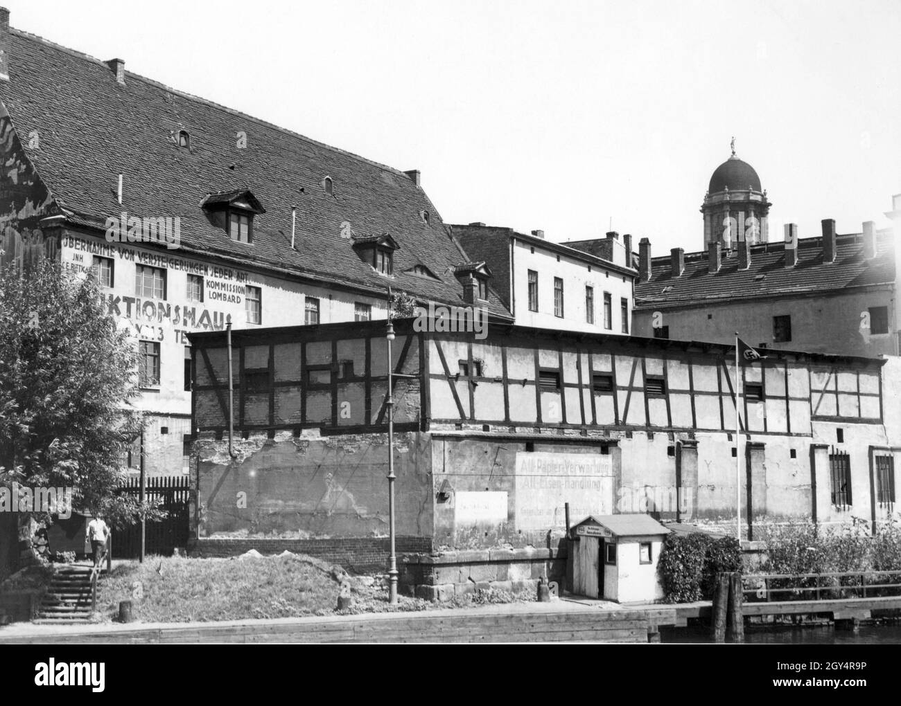 'In July 1934, the last city tour took place through the alley Am Krögel in Berlin-Mitte, whose buildings were demolished shortly afterwards. The picture shows some of the houses that were located near the Old Town House (tower in the background), including a warehouse for ''Alt-Papier-Verwertung, Alt-Eisen-Handlung'' and the auction house of owner C. E. Bittkar with ''Übernahme von Versteigerungen jeder Art. Commission Lombard''. [automated translation]' Stock Photo