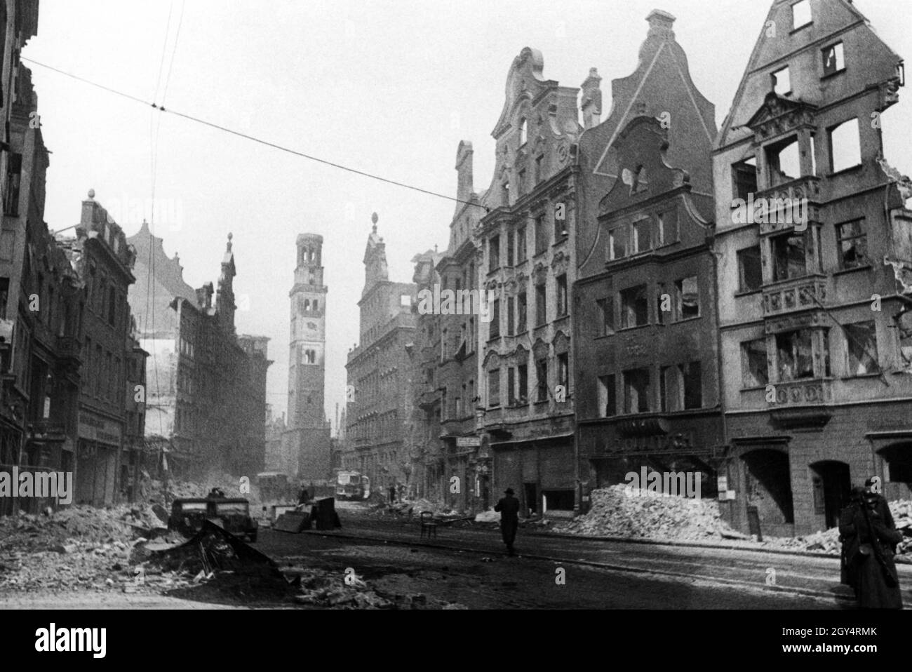 The photograph shows Maximilianstraße in Augsburg in the last years of the Second World War. Many houses are completely bombed out after air raids. In the background you can see the damaged Perlachturm and the town hall (to the right). On the right side of the picture three soldiers of the Wehrmacht are crossing the street. [automated translation] Stock Photo