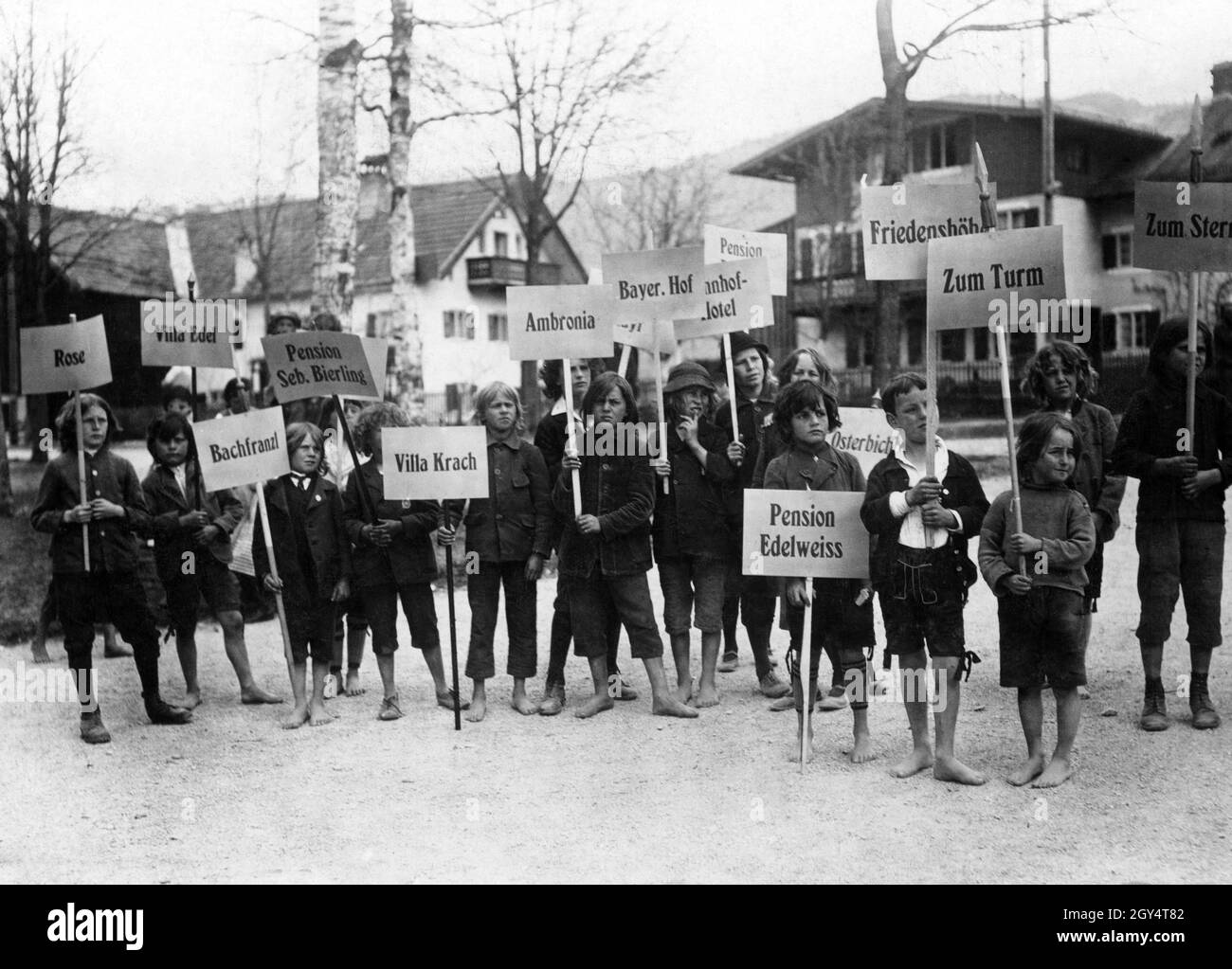 The guests arriving for the Passion Play in May and June 1922 were welcomed by a crowd of children. Each child carries a sign of an accommodation in Oberammergau to take the guests there. The accommodations include (from left to right): Rose, Villa Edel, Bachfranzl, Pension Seb. Bierling, Villa Krach, Ambronia, Bayer. Hof, Pension Edelweiss, Osterbichl, Friedenshöhe, Zum Turm, Zum Stern. [automated translation] Stock Photo