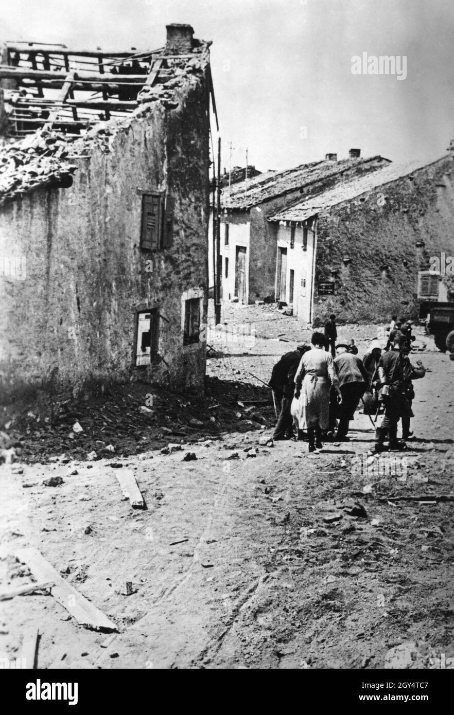 A small group of French refugees walk through a town whose houses have been destroyed by bombing. [automated translation] Stock Photo