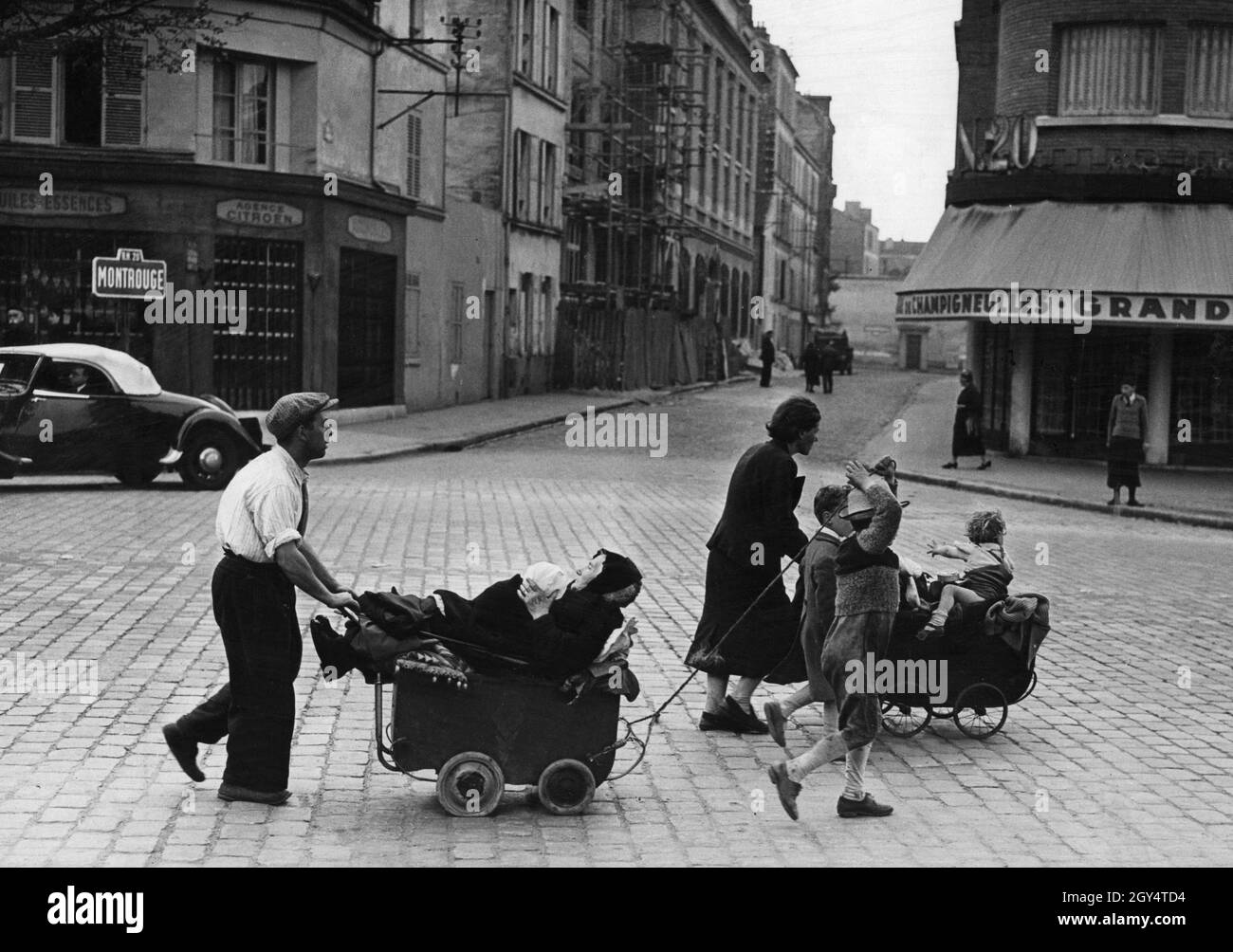 A family walks with their belongings through the streets of Paris at the Porte  d'Orléans. A street sign on the left indicates the Montrouge district.  [automated translation] Stock Photo - Alamy