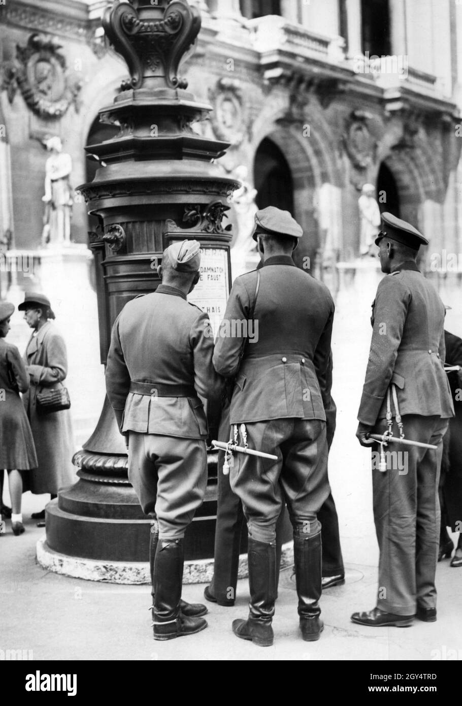 'Soldiers of the German Wehrmacht look at a poster advertising the opera performance of ''La Damnation de Faust'' in occupied Paris. [automated translation]' Stock Photo