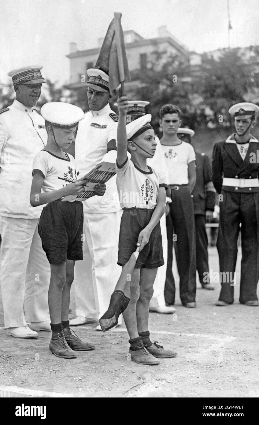 Two boys from the Italian Opera Nazionale Balilla rehearse military commands in 1933. Behind the children are an admiral of the Italian navy (left) and an officer. [automated translation] Stock Photo