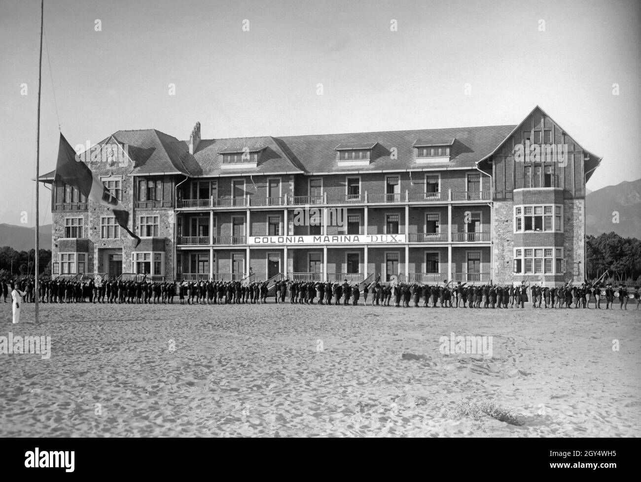 'The Italian youth organization Opera Nazionale Balilla ran youth hostels like this Colonia ''Dux'' right on the beach near Marina di Carrara. In the picture from 1931, Balilla groups are lined up for roll call while the Italian flag is hoisted. [automated translation]' Stock Photo