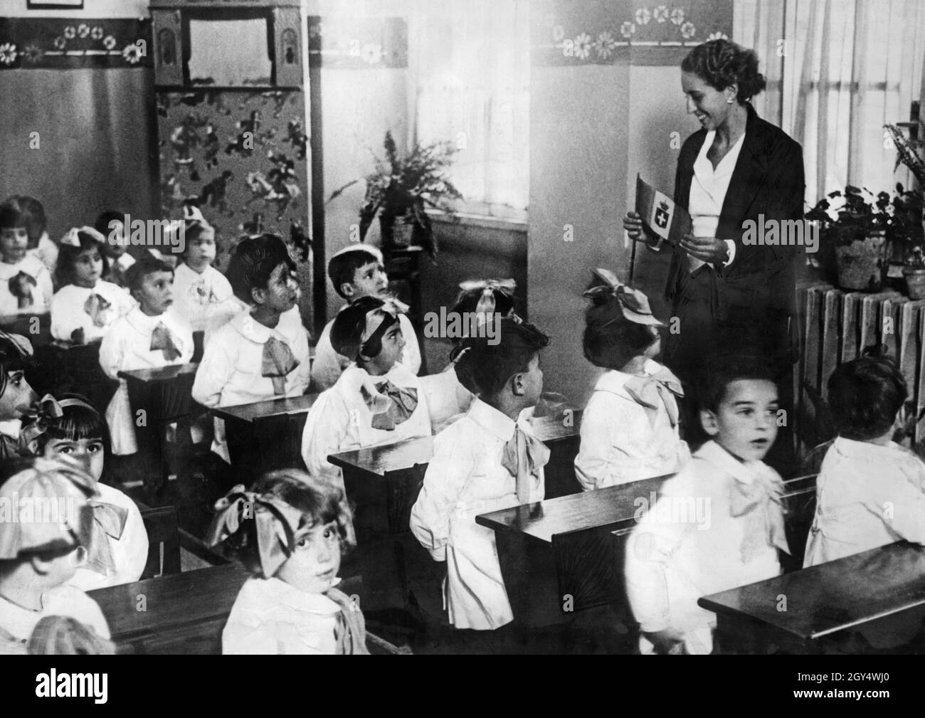 In fascist Italy, uniform uniforms were first introduced for pupils, then also for teachers (from about 1934). The picture was taken in 1934 at a primary school in Rome and shows the school uniforms. The teacher is explaining the flag of Italy to her class. [automated translation] Stock Photo