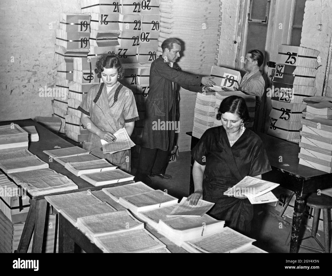 Binding the telephone directories for the year 1937: Workers carry the individual pages together. In the background, the stacks with the finished printed sheets delivered by the Reichsdruckerei. [automated translation] Stock Photo