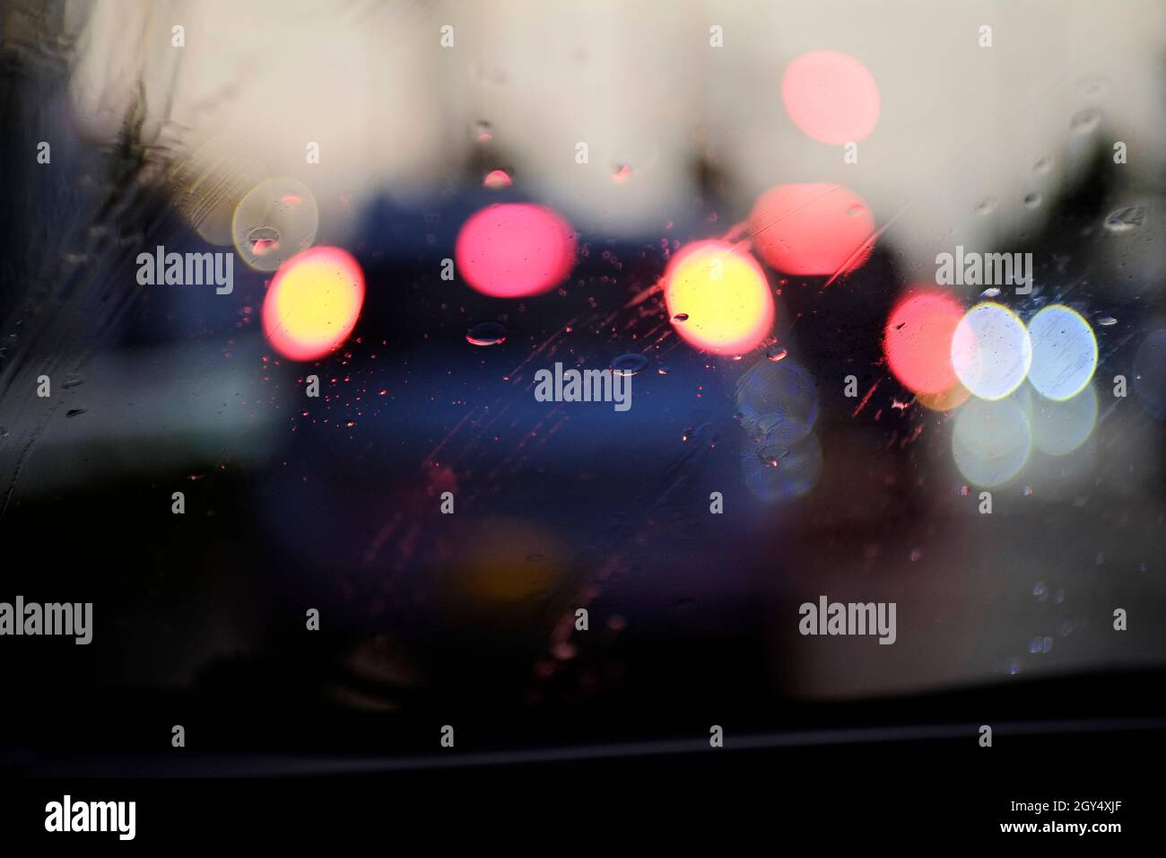 Rain drops on the windshield and bokeh lights from the cars in front. Abstract picture. Stock Photo