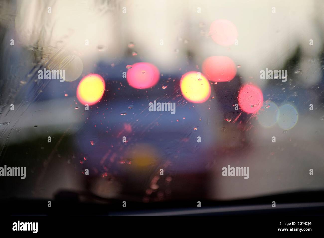 Rain drops on the windshield and bokeh lights from the cars in front. Stock Photo