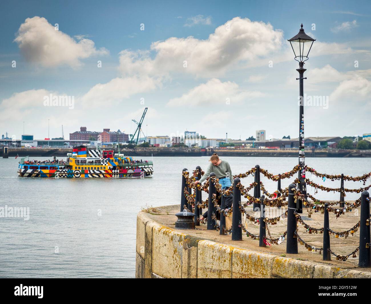 1 September 2021; Liverpool, Merseyside - A young woman looks at padlocks strung on chains on the Liverpool waterfront, while the Mersey ferry 'Snowdr Stock Photo