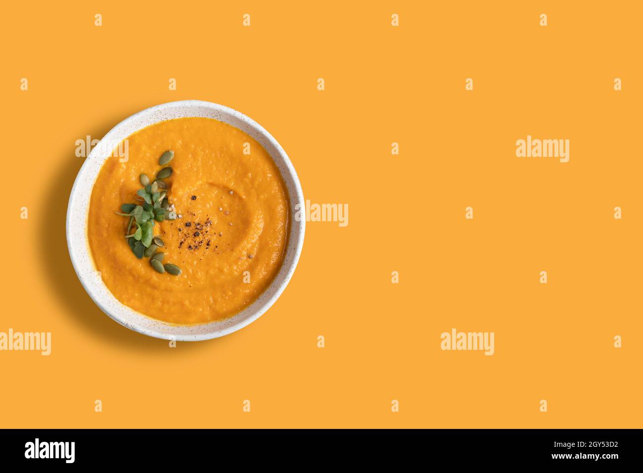 Pumpkin soup decorated microgreens amd pumpkin seeds isolated on orange background. View from