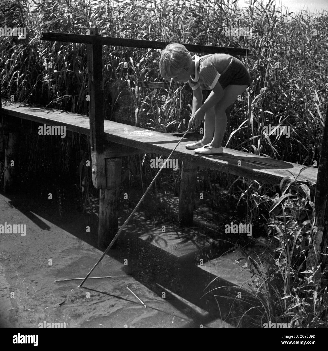 Ein kleiner Junge spielt gedankenverloren an einem Steg mit einem Stock, Deutschland 1930er Jahre. A little boy, lost in thoughts, playing at a grouser, Germany 1930s. Stock Photo