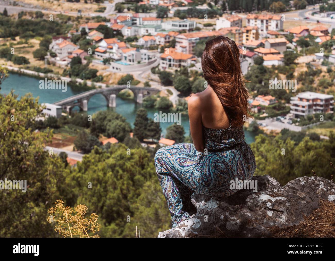 Handsome girl sitting on a cliff with an amazing view of Arslanagic/Perovic bridge in Treebinje Stock Photo