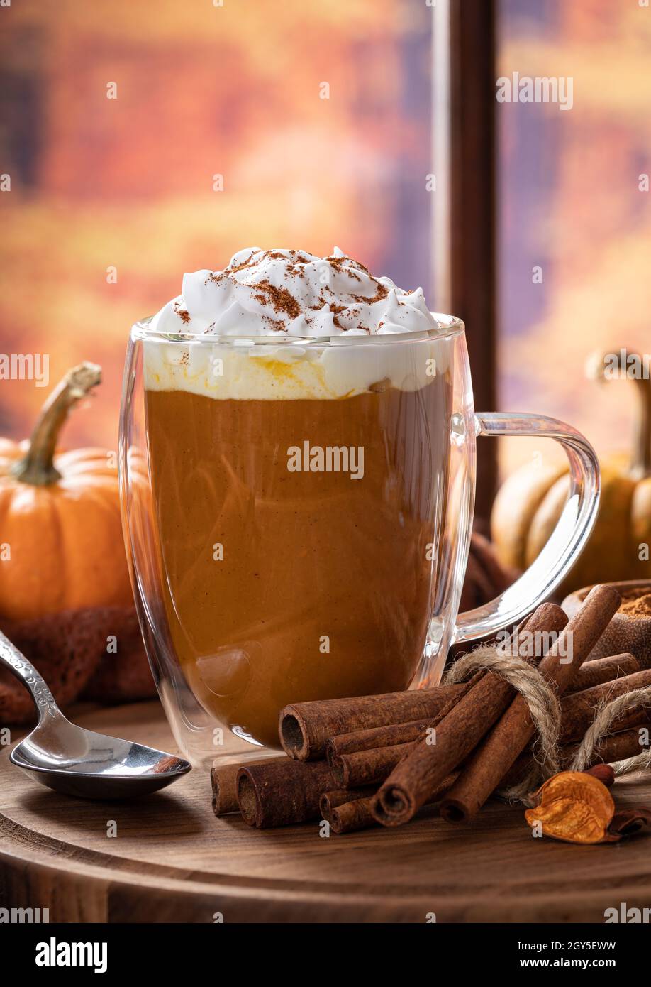 Pumpkin spice latte with cinnamon sticks and pumpkins by a window with ...