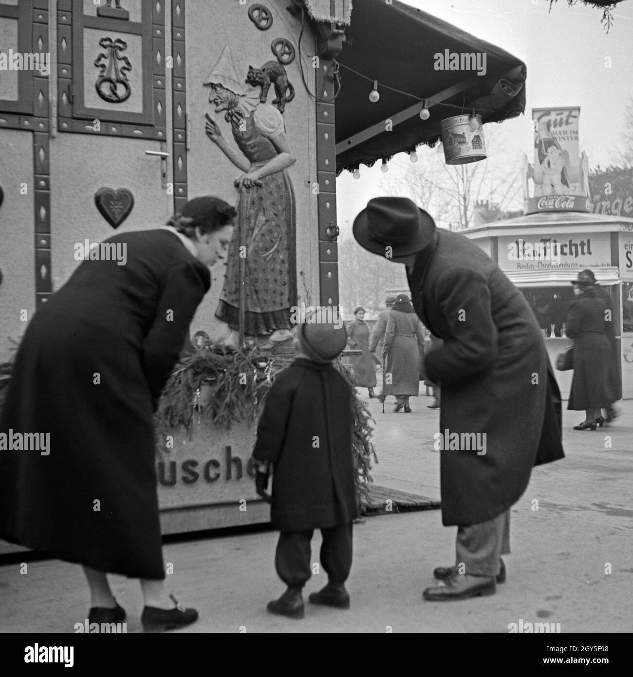 Ein kleiner Junge bestaunt mit seinen Eltern die Hexe am Knusperhaus Süßwarenstand auf dem Weihnachtsmarkt, Deutschland 1930er Jahre. A little boy and his parents gazing at a witch relief of the candy booth at the christmas market, Germany 1930s. Stock Photo
