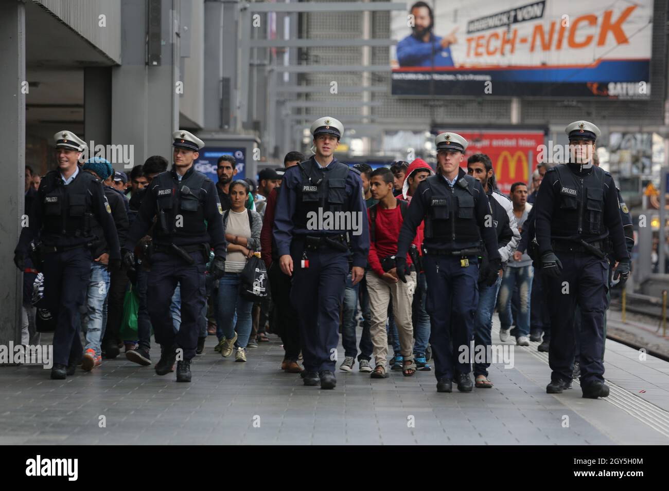 German police officers lead newly-arrived immigrants through Munich Central station. Stock Photo