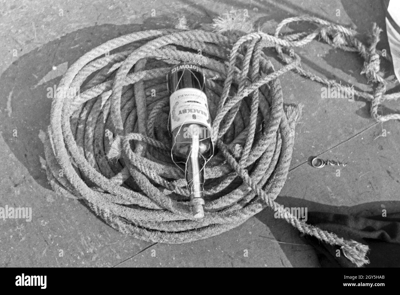 Eine Flasche Rum zwischen den Tauen auf Deck, Deutschland 1930er Jahre. A bottle of rum between ropes on deck, Germany 1930s. Stock Photo