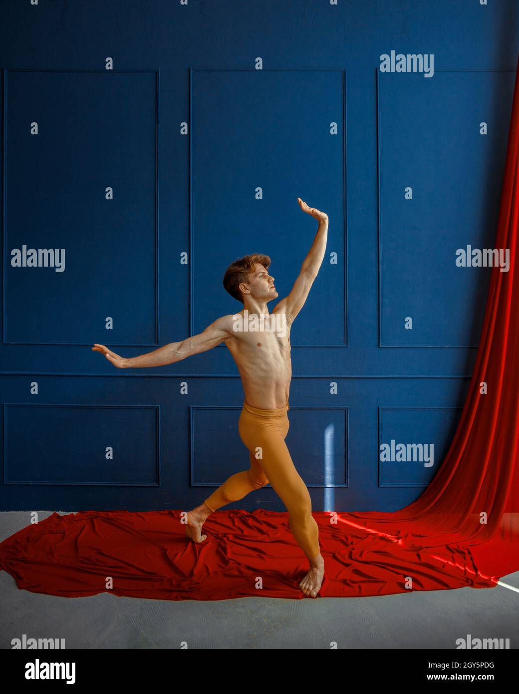 Male ballet dancer, performing in action, dancing studio, blue wall and