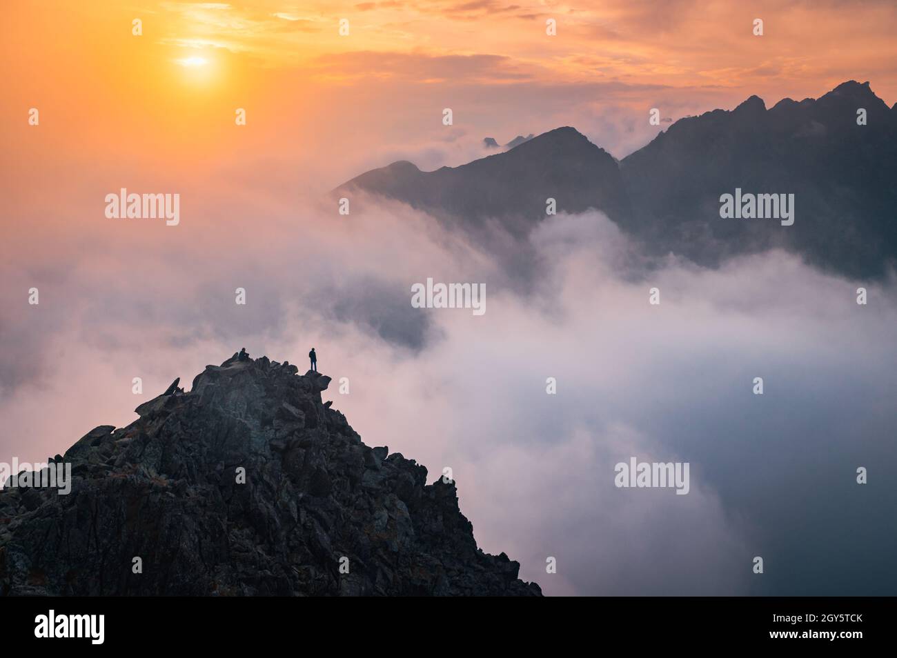 Hiker with open arms at the top of the hill. Beautiful sunset light and mist in background. Mountains scenery. Edit space. Stock Photo