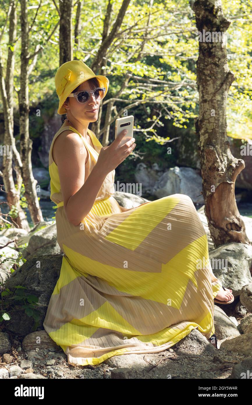 Beautiful woman sitting in the woods with a yellow dress and a phone Stock Photo