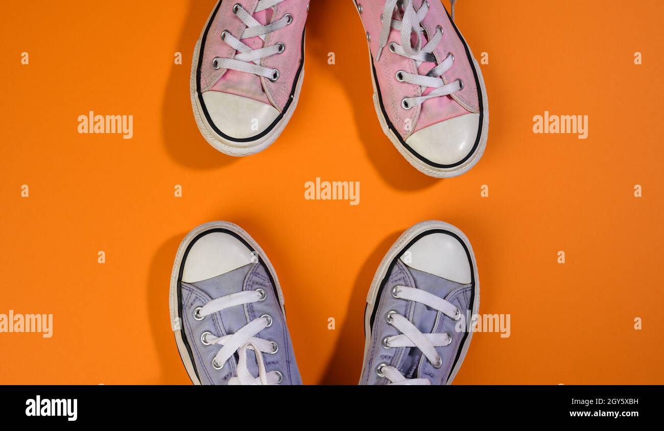 two pairs of textile sneakers on an orange background stand opposite each other. Dialogue and confrontation concept, top view Stock Photo