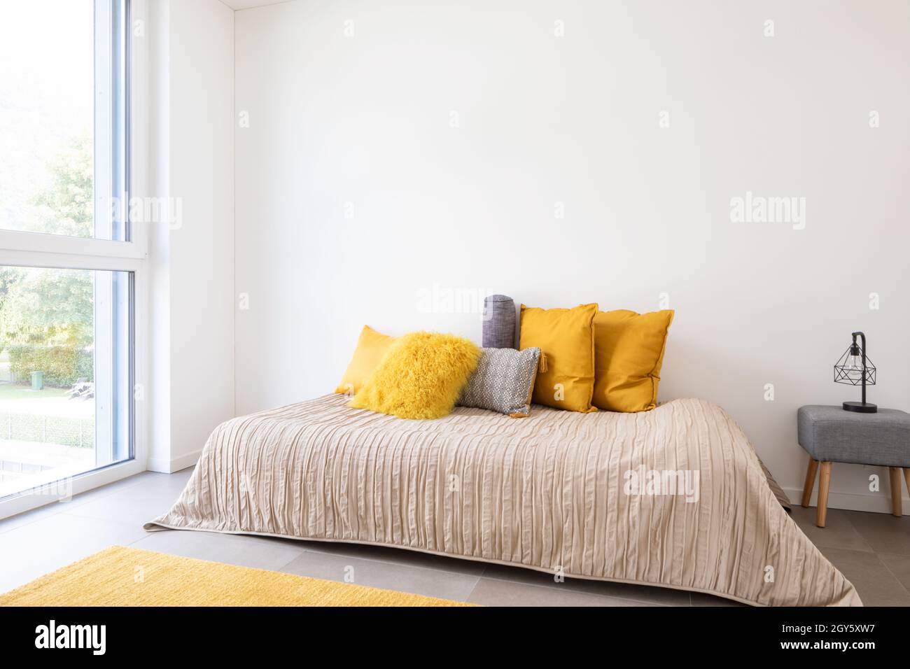 Nice bedroom with a bed, sidetable and lots of pillows. Detail of the bed with a large white wall, perfect for copy space. Very romantic room. Concept Stock Photo