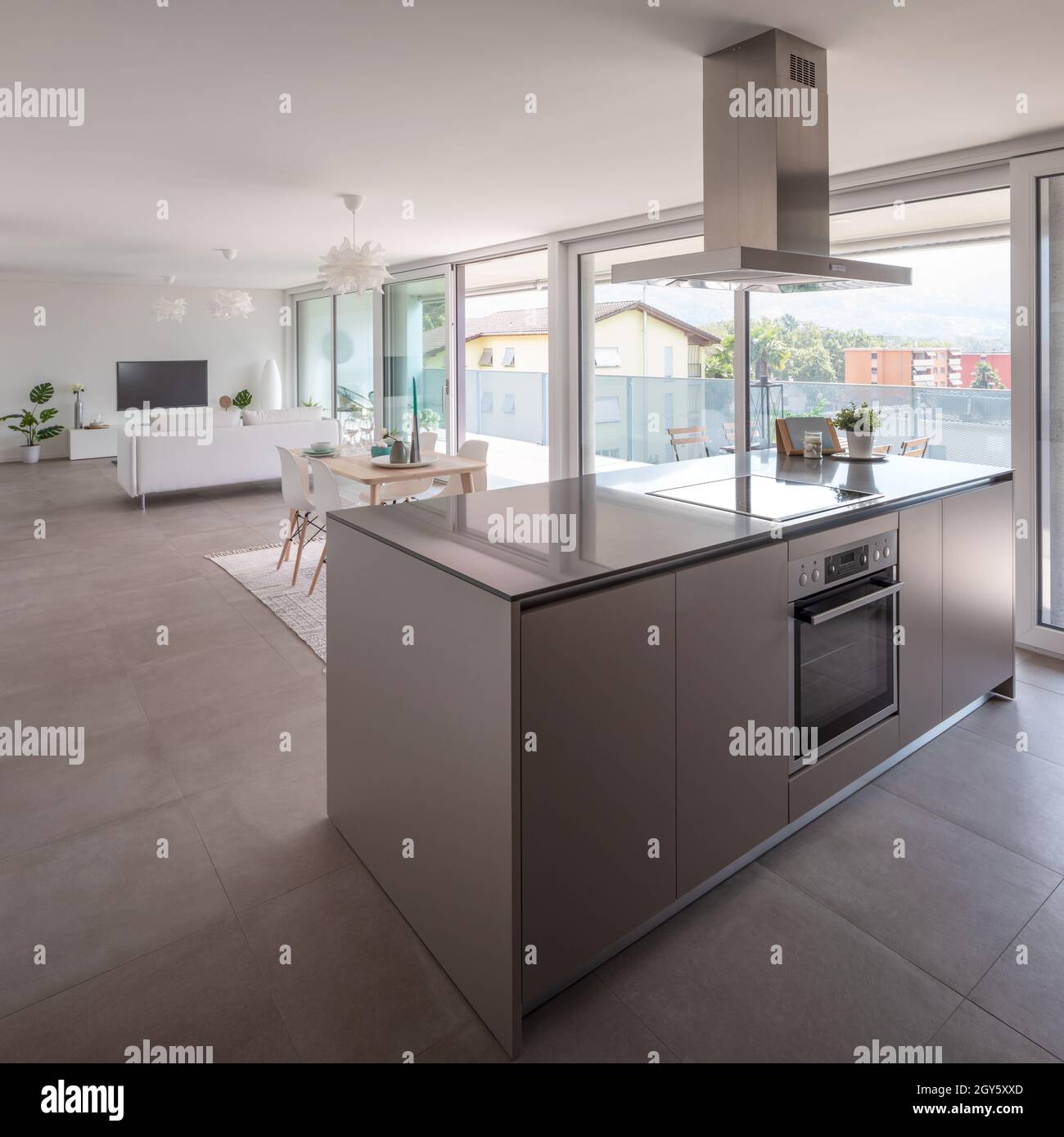 Modern kitchen with island, oven, induction plate and hood. Behind the table and sofa. Nobody inside Stock Photo