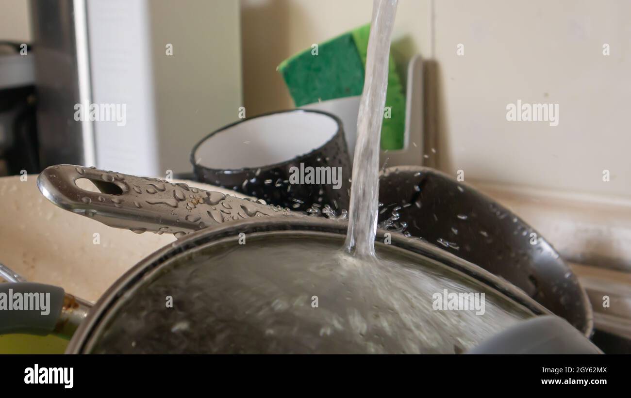 The kitchen utensils in the wash basin need to be washed. A pile of dirty dishes in the kitchen sink with running water. Kitchen utensils need washing Stock Photo