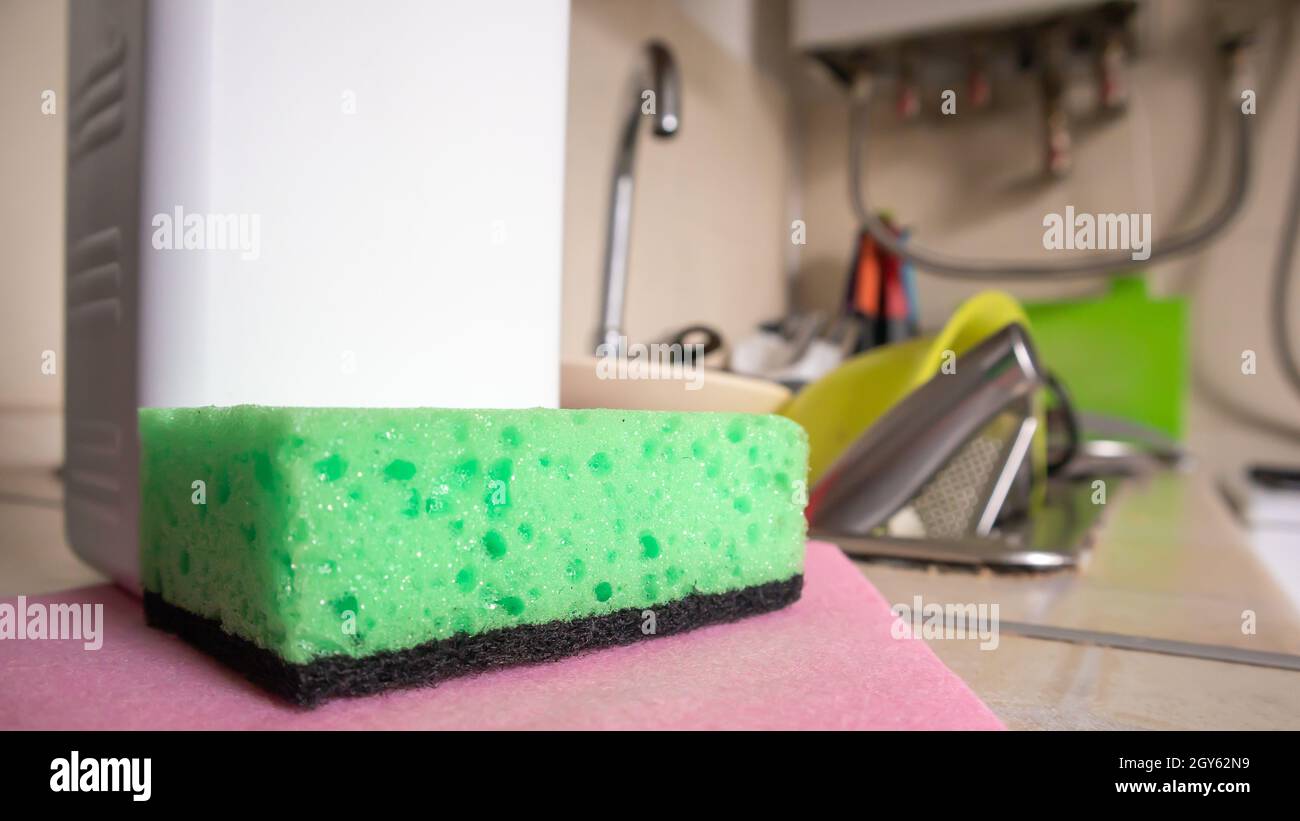 Green sponge and liquid soap dispenser for washing dishes on a dirty sink completely with dishes and kitchen utensils. Washing dishes in the kitchen b Stock Photo