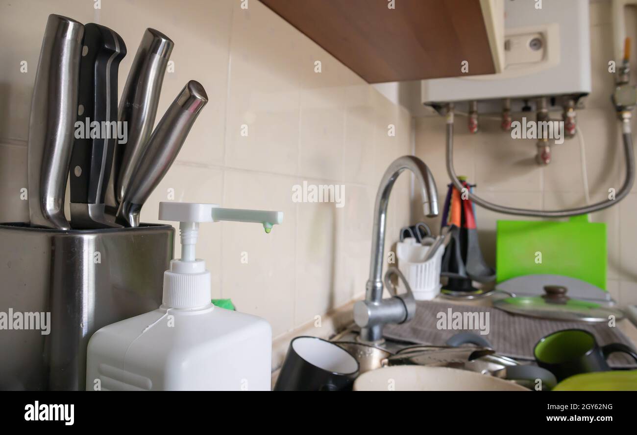 Green sponge and liquid soap dispenser for washing dishes on a dirty sink completely with dishes and kitchen utensils. Washing dishes in the kitchen b Stock Photo