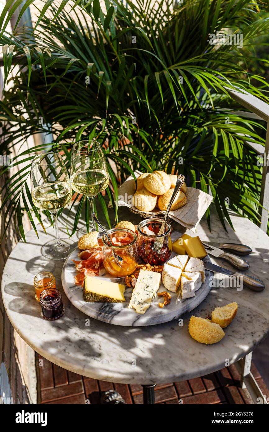 Varied appetizer Cheese plate with soft cheese, fruit sauce and white wine on marble table for small party on summer sunny day Stock Photo