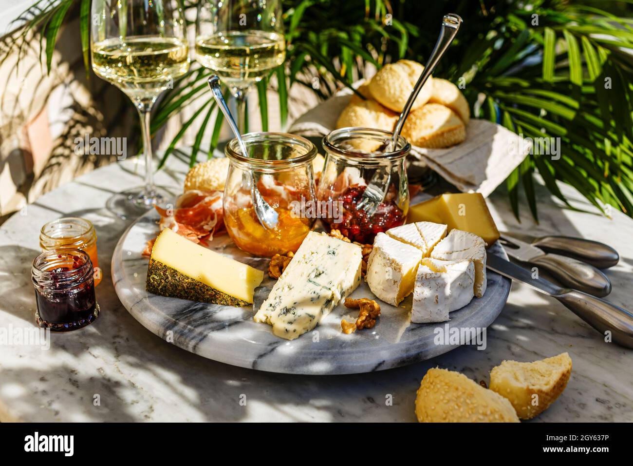 Varied appetizer Cheese plate with soft cheese, fruit sauce and white wine on marble table for small party on summer sunny day Stock Photo