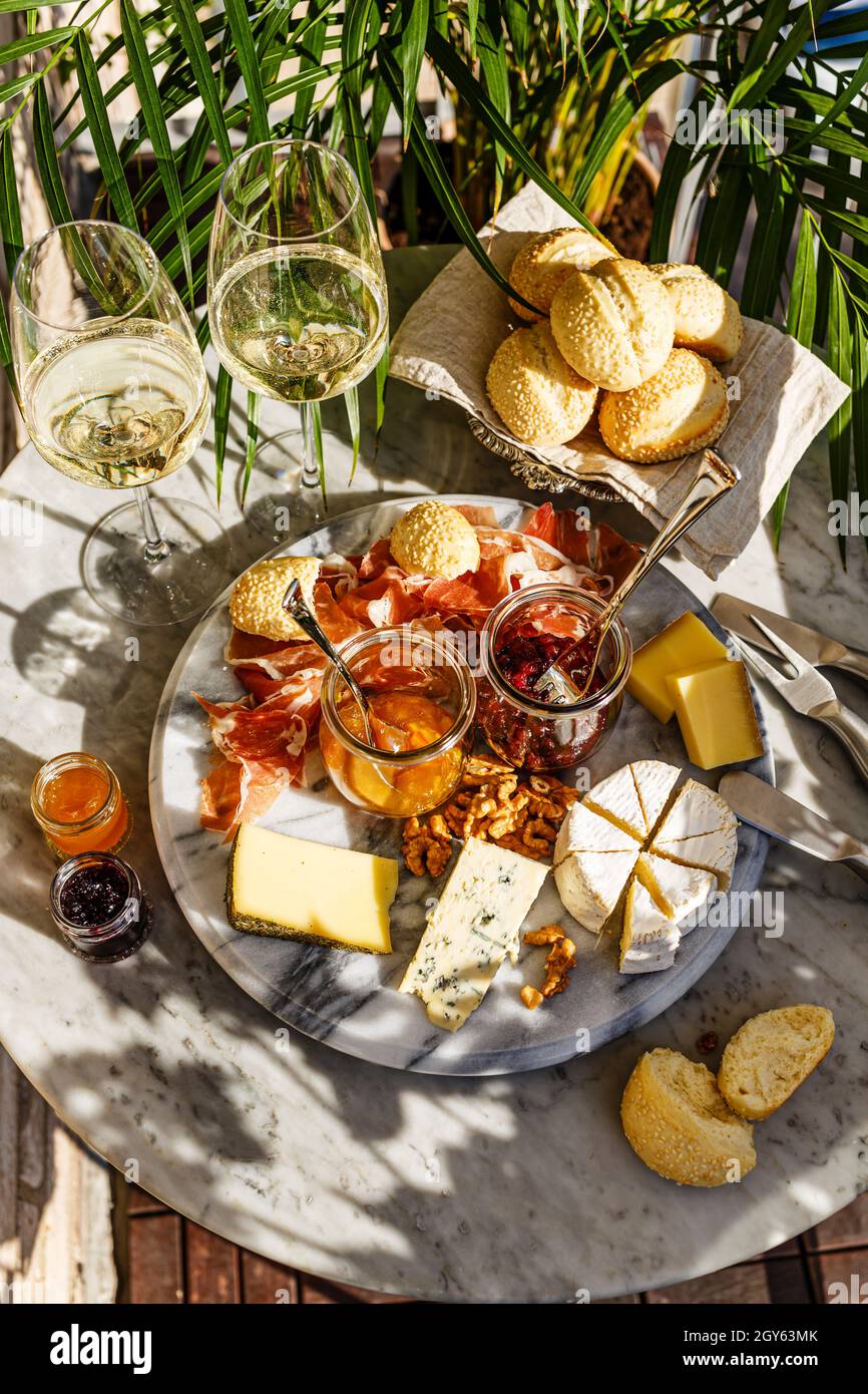 Varied appetizer Cheese plate with soft cheese, fruit sauce and white wine on marble table for small party on summer sunny day Stock Photo