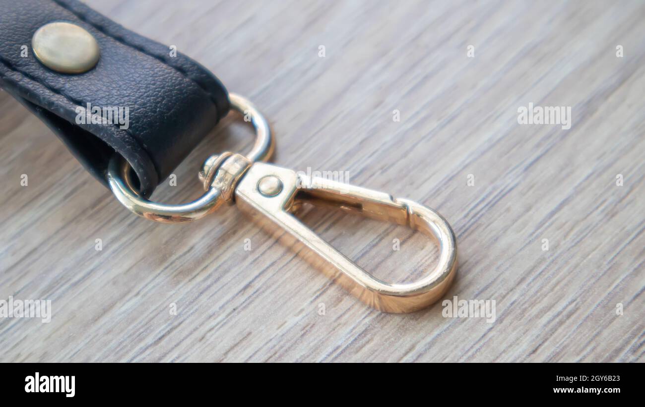 Swivel carabiner fastener with leather black bag strap on a wooden