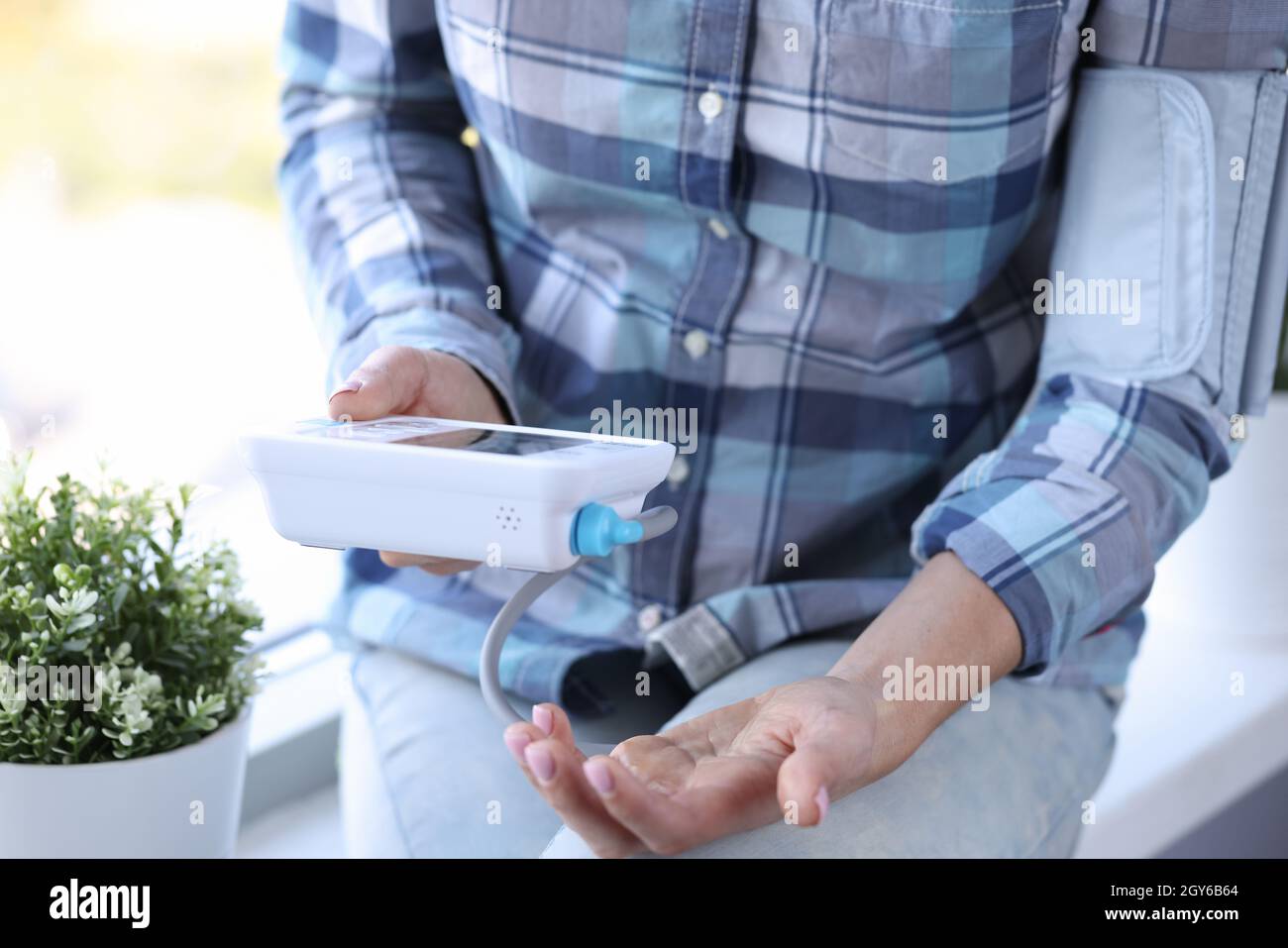 Woman measures blood pressure with automatic tonometer while sitting on windowsill Stock Photo