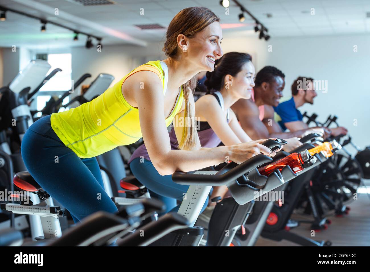 Very fit Caucasian woman and her friends on fitness bike in gym Stock Photo