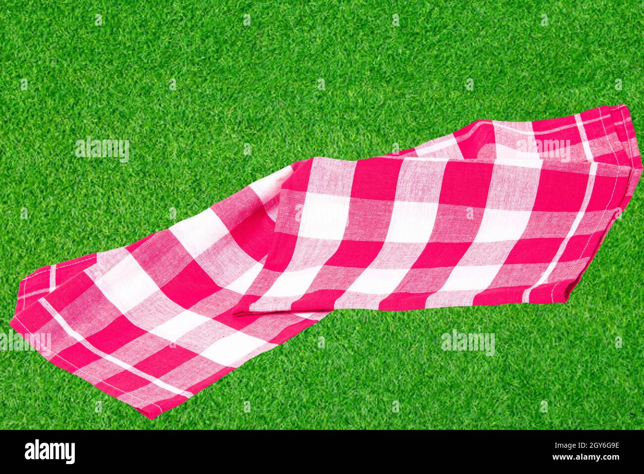Red picnic blanket. Red checkered picnic cloth on blurred sunflooded lush grass with focus on